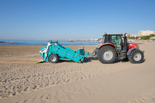 red tractor with green trailer cleaner cleaning sand of Beach Els Terrers, in Benicassim, Castellon, Valencia, Spain, Europe. Mediterranean Sea
