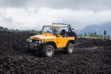 Offroad yelow vehicle parked at the top of a valley with volcanic rock and mountains in Bali,...