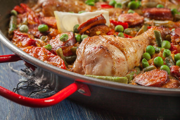 Traditional paella with chicken legs, sausage chorizo and vegetables served in paellera