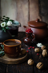 Obraz na płótnie Canvas brown cup of coffee on a wooden plate with nuts, red currant in a small pot, white flowers and brown pot on a backside on a brown wooden table