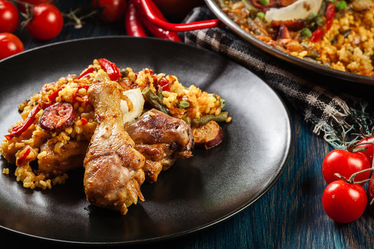 Traditional paella with chicken legs, sausage chorizo and vegetables served on black plate