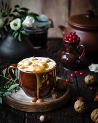 iced coffee with ice cream and caramel in a brown cup on a wooden plate with nuts, red currant in a pot on a brown wooden table