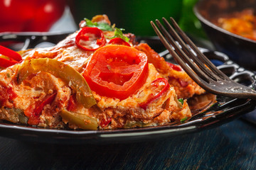Portion of frittata with eggs, sausage chorizo, red pepper, green pepper, tomatoes, cheese and chili in a plate on wooden table.