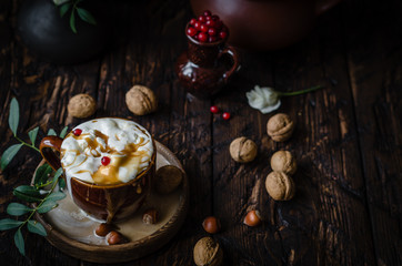 iced coffee with ice cream and caramel in a brown cup on a wooden plate with nuts, red currant in a pot on a brown wooden table