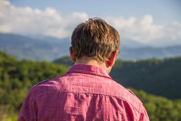 Young man in pink shirt from back enjoying beautiful mountain view