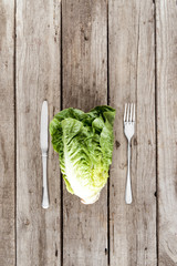 top view of fresh letuce salad with fork and knife on wooden table, healthy eating concept