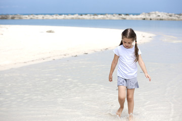 Happy child on the beach. Paradise holiday concept, girl seating on sandy beach with blue shallow water and clean sky