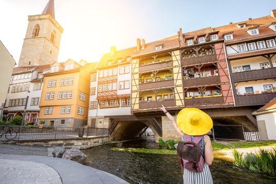 Young woman tourist in yellow hat standing back on the famous Merchants bridge background in Erfurt city, Germany