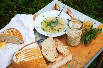 Barley soup, loaf of bread, barley in glass on cracked old table in garden.