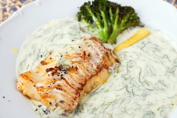 Roasted cod fish in dill sauce, portion on white.