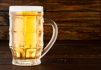 glass of cold frothy lager beer on old wooden table