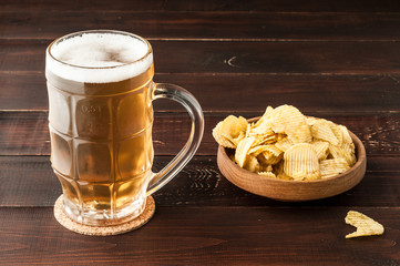 glass of cold frothy lager beer and potato chips plate on wooden table