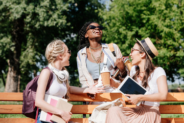 multicultural cheerful women resting on bench in park together
