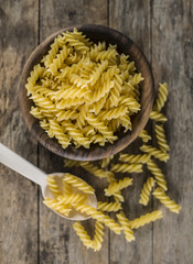 Pasta fusilli in a wooden bowl on wood background for healthy recipes.
