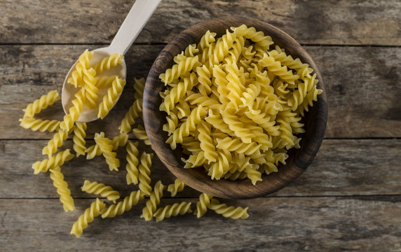 Pasta fusilli in a wooden bowl on wood background for healthy recipes.