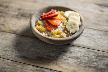 oatmeal porridge with strawberry and banana in wood bowl