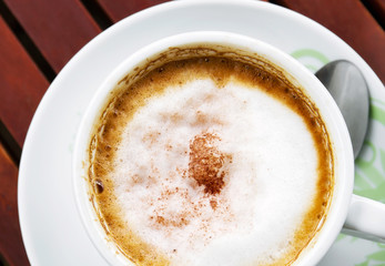 Top view of cappuccino coffee cup with silver spoon on wooden table
