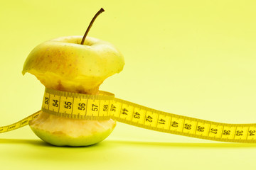 Flexible ruler in yellow color ties around bitten apple