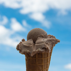 Scoop of ice in cone, close up against blue sky with clouds