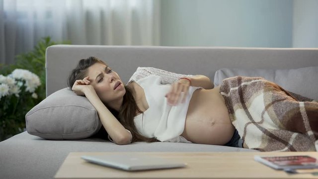 Pregnant lady lying on sofa, having sudden vomiting urge, breathing to calm down