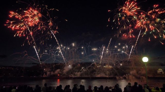 Firewok bombs are bursting in air. Crowds of people are looking at fireworks. 4K.