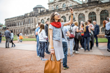Young smiling woman photographing with smartphone while visiting with tourist group the old palace in Dresden city, Germany - obrazy, fototapety, plakaty
