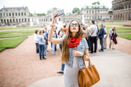 Young smiling woman photographing with smartphone while visiting with tourist group the old palace in Dresden city, Germany