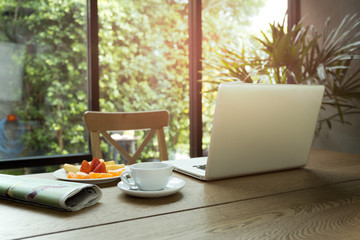 Cup of coffee and fresh fruit with newspaper on the table and laptop computer