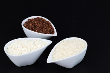 3 kind of raw Thai rice Thai Jasmine rice(Hom Mali ), Glutinous/Sticky Rice (Khao Neow), Brown Rice (Khao Dum) in white cups on black background with copy space