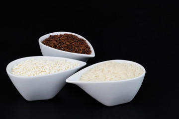 3 kind of raw Thai rice Thai Jasmine rice(Hom Mali ), Glutinous/Sticky Rice (Khao Neow), Brown Rice (Khao Dum) in white cups on black background with copy space
