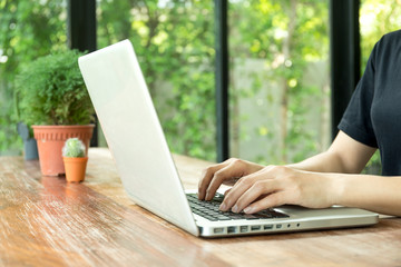 Woman's hands typing on laptop's keyboard on wooden table