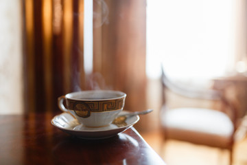 The smell of coffee in vintage mugs, couple in an expensive interior on the background of the window. Mug with pattern on saucer and spoon