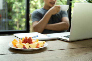 Obraz na płótnie Canvas Selected focus fresh fruit with man holding cup of coffee looking at laptop