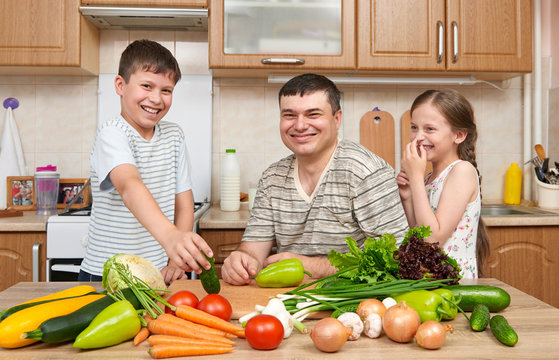 Father and two children in home kitchen interior. Happy family, girl and boy having fun with fruits and vegetables. Healthy food concept.