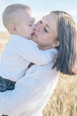 adorable baby boy kissing his pretty young mather outdoor at summer day. Family dressed in national white clothes