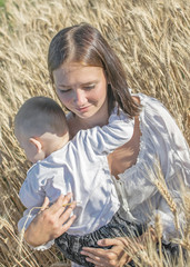 Young beautiful mother and baby boy hugging in wheat field