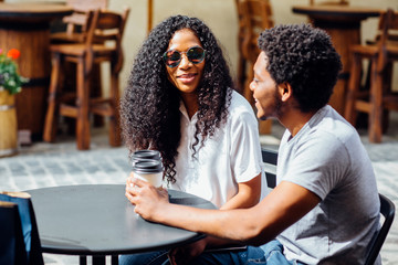 Young romantic afro-indians couple drinking coffee in a cozy outdoor cafe - summer holidays and vacation concept.