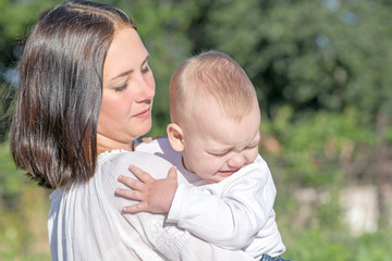 Portrait of a crying little baby boy and yound mother calming him