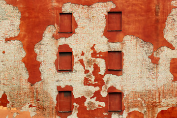 Boarded windows in old brick wall covered with red flaking plaster