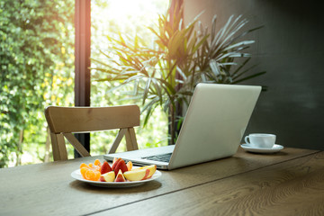 Wooden desk with fresh fruits and laptop with green plant