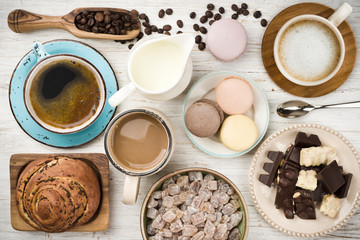 Coffee cup, beans, chocolate, macaroons, milk, bun, sugar on wood