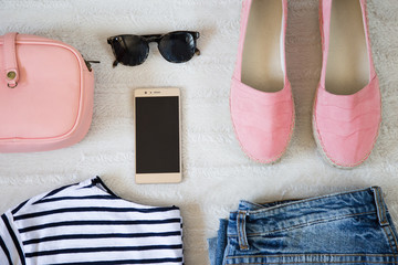 perfect summer outfit accessories. flat lay of a trendy woman fashion outfit. denim jeans, striped shirt, pink espadrilles shoes, pink bag, sunglasses and a elegant smartphone. top view.