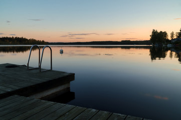 Naklejka na ściany i meble Calm summer evening sunset, jetty with ladder in reflection lake