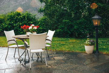 Beautiful terrace or balcony with small table, chairs and flowers after rain