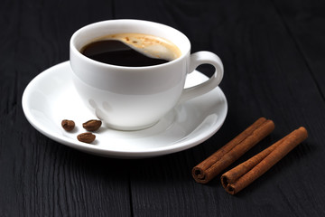 Black coffee in a white cup with cinnamon and foam on a black wooden background