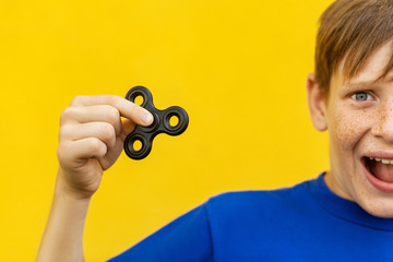 Young beautiful happy boy with freckles blue t-shirt holding fidget spinner on yellow background...