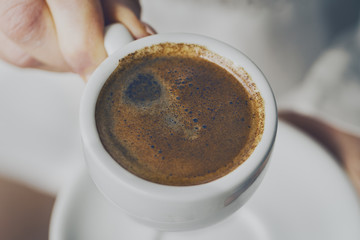 Closeup of tasty coffee espresso with tasty foam in small ceramic cup. Male hands holding warm hot drink.