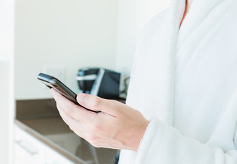 Man in a bathrobe using his smartphone indoors