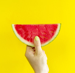 Beautiful feminine hands holding fresh tasty red appetizing watermelon on bright yellow background. Summer Concept.