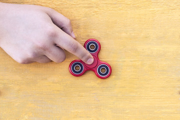 Closeup of a young caucasian man playing with a new red fidget spinner on a yellow wooden background